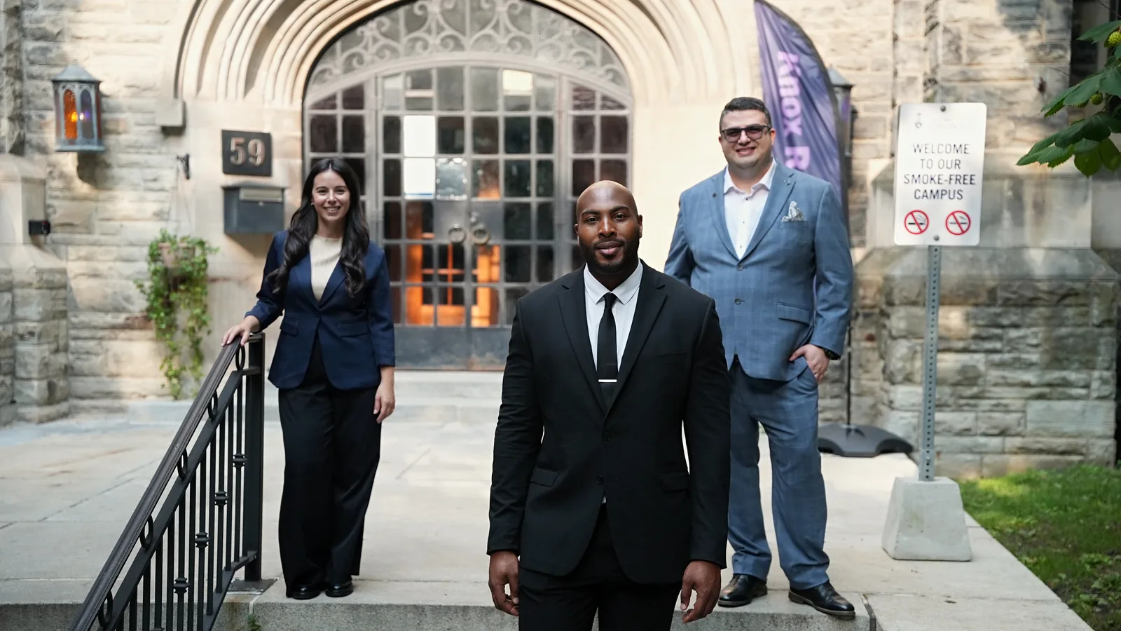 Three professionals standing at the entrance of a historic stone building on a Toronto campus.