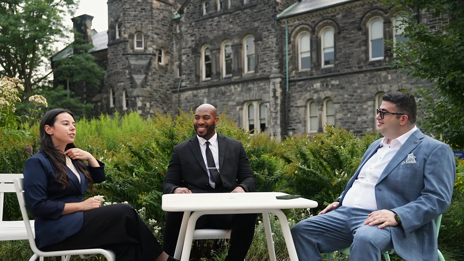 Three professionals in conversation around a small outdoor table beside a historic stone building in Toronto.
